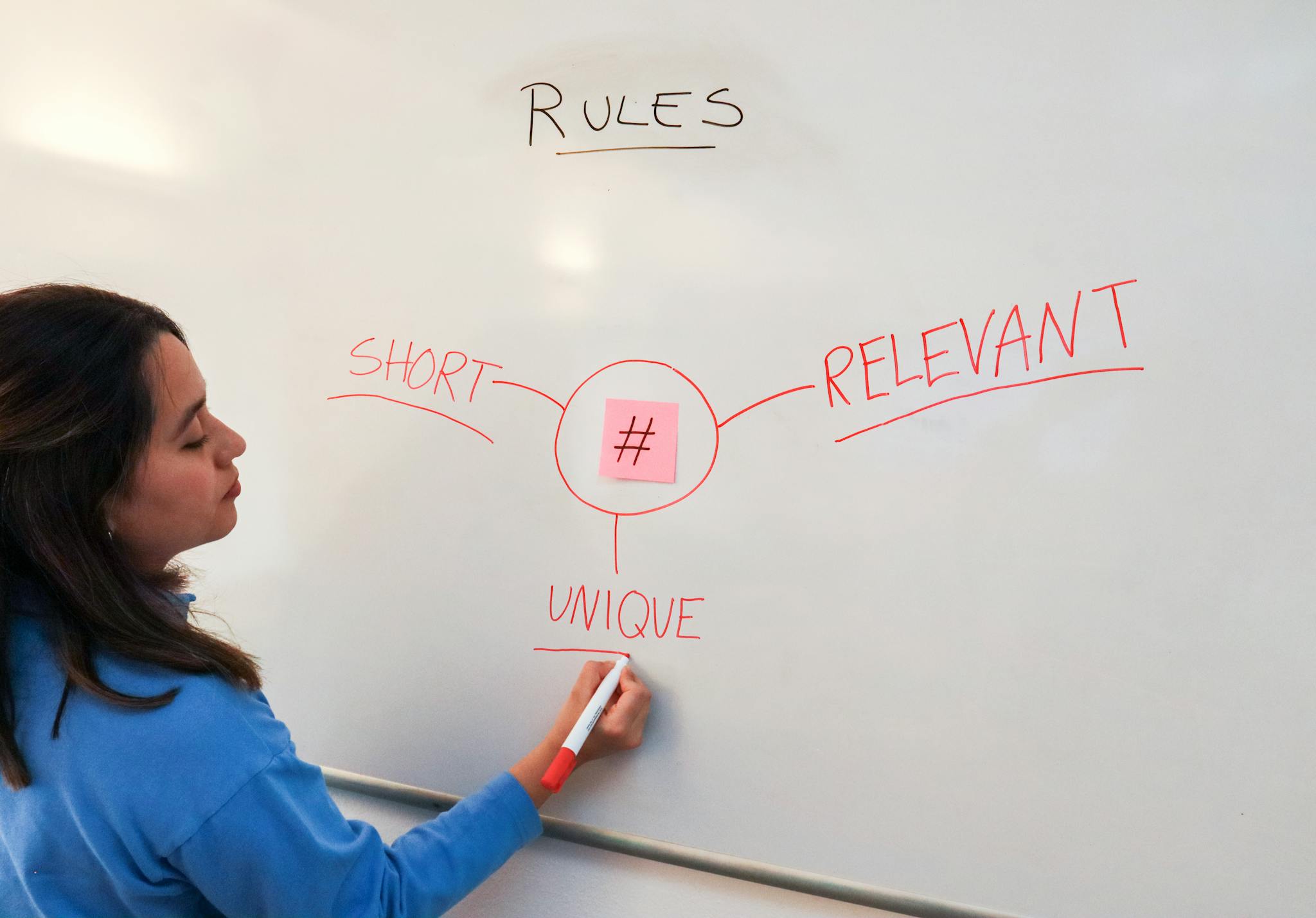 Woman illustrating marketing rules with hashtags on a whiteboard for effective branding strategies.